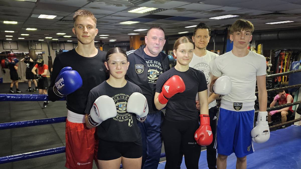 Grupa młodych bokser&oacute;w i ich trener&oacute;w pozuje do zdjęcia w sali treningowej, niekt&oacute;rzy trzymają rękawice bokserskie.