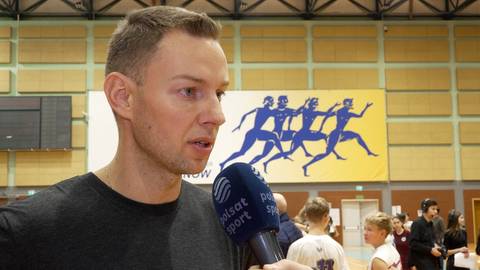 Mężczyzna m&oacute;wi do mikrofonu z logo Polsat Sport. W tle grupa dzieci.