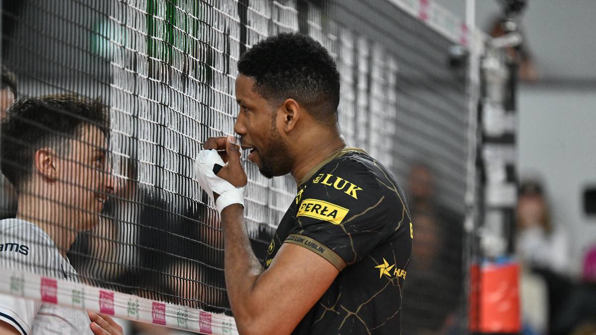 Siatkarz w czarnej koszulce z napisem "LUK" rozmawia z zawodnikiem w białej koszulce przez siatkę.