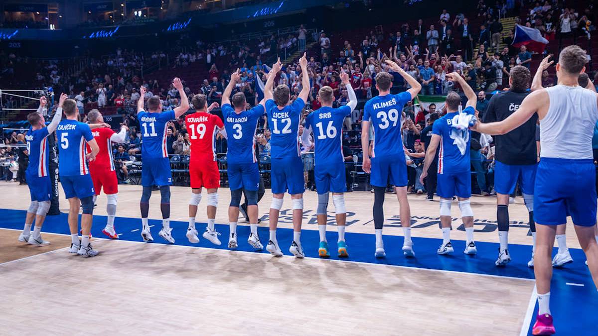 Grupa siatkarzy w niebieskich koszulkach z numerami na plecach, stoi w rzędzie na boisku, z rękami w górze, celebrując.