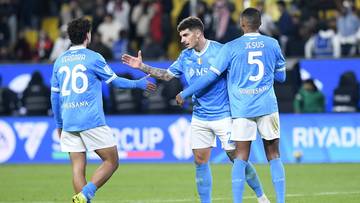 Trzech piłkarzy w niebieskich strojach celebruje zdobycie bramki na boisku.