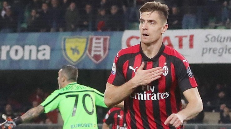 Piłkarz w koszulce AC Milan z ręką na piersi i uśmiechem.