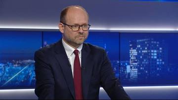 Mężczyzna w okularach i garniturze w studiu telewizyjnym.