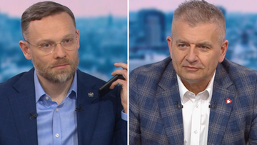 Dw&oacute;ch mężczyzn w studiu telewizyjnym, jeden z nich trzyma w dłoni telefon.
