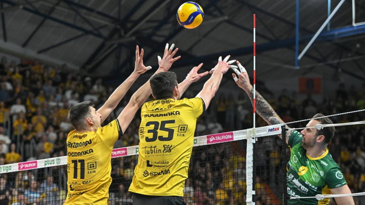 Trzech siatkarzy podczas meczu. Dwóch graczy w żółtych strojach próbuje zablokować atakującego przeciwnika w zielonym stroju.