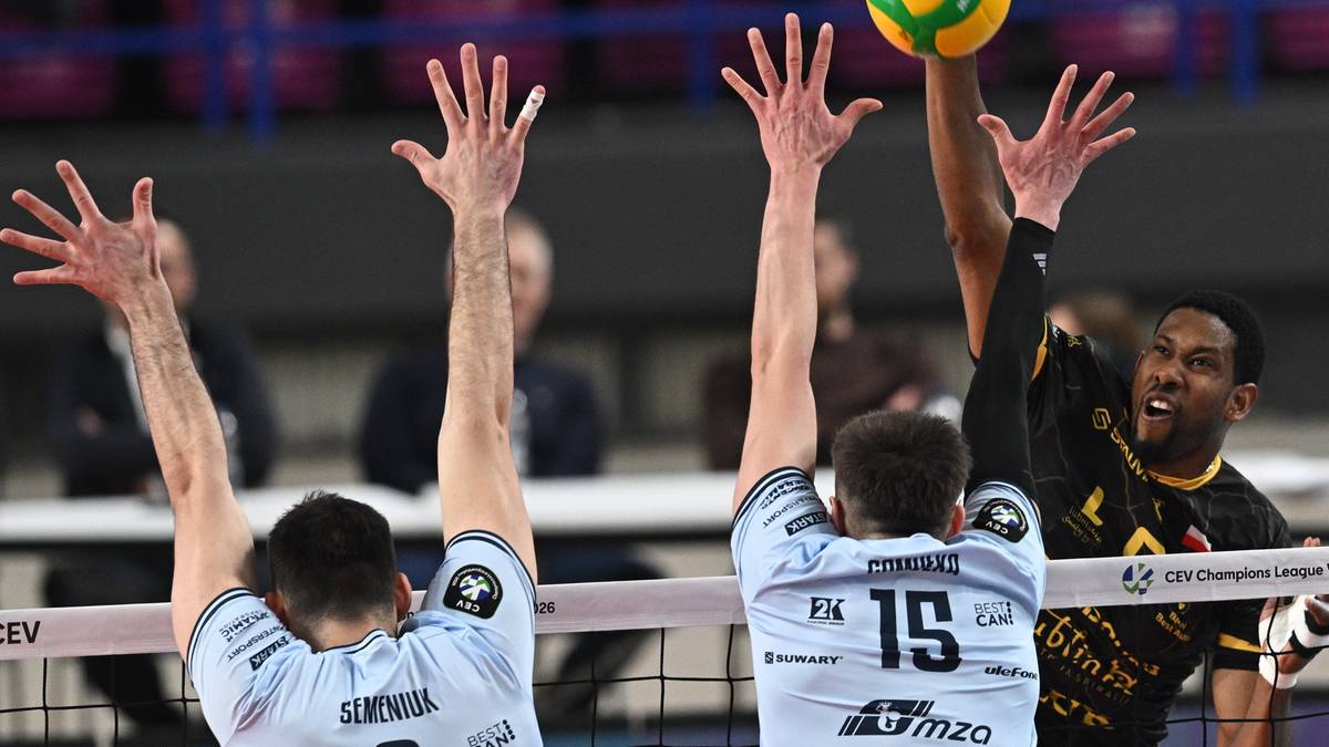 Siatkarze walczący przy siatce, jeden z nich uderza piłkę nad blokiem dw&oacute;ch przeciwnik&oacute;w.