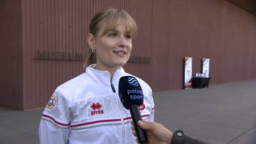 Kobieta w białej kurtce sportowej udziela wywiadu, trzymając mikrofon.