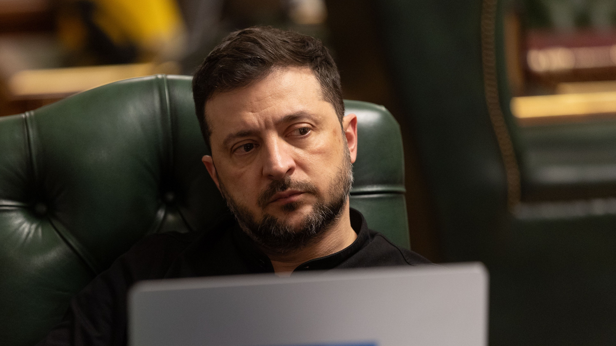 Wołodymyr Zełenski, prezydent Ukrainy, siedzi w fotelu i patrzy na ekran laptopa z logo Ukrainy.