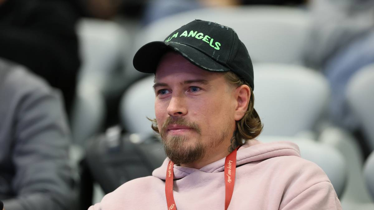 Mężczyzna z zarostem w czarnej czapce z napisem "Palm Angels" i r&oacute;żowej bluzie siedzi na widowni.