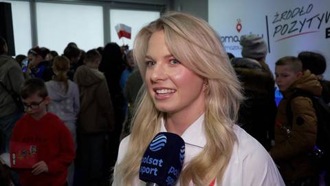Karolina Bosiek z mikrofonem Polsat Sport, uśmiecha się do kamery, w tle tłum ludzi i napis "ŹR&Oacute;DŁO POZYTYWNYCH EMOCJI".