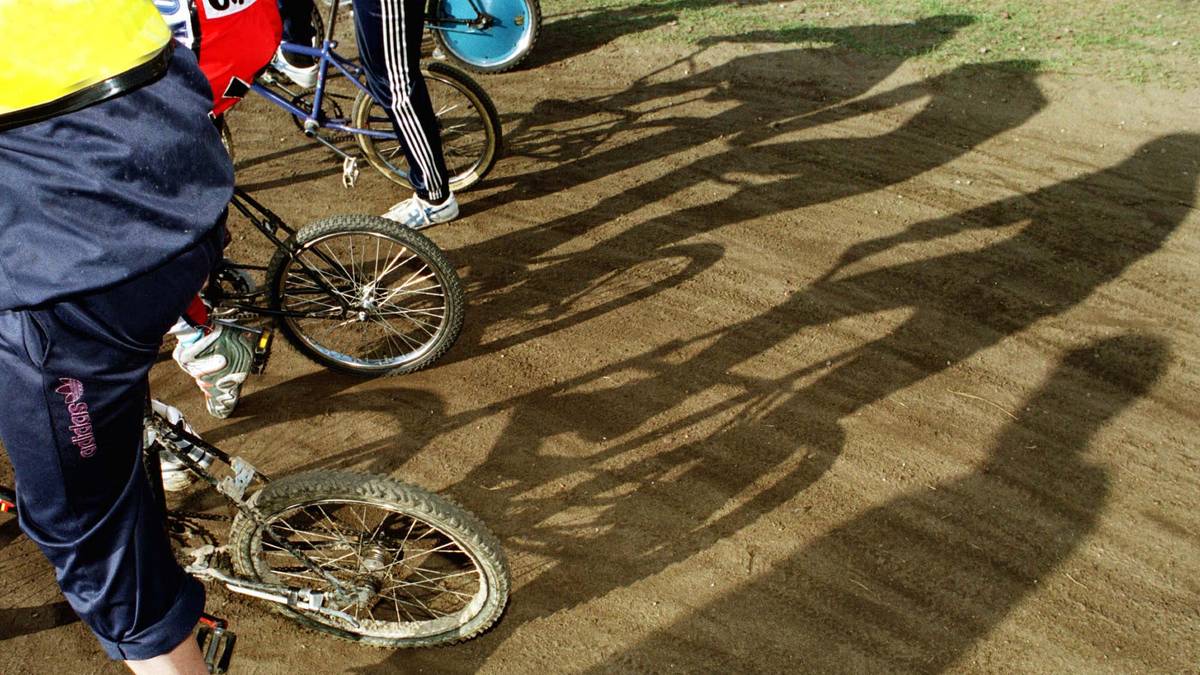Fragmenty n&oacute;g zawodnik&oacute;w i rower&oacute;w na torze, rzucających długie cienie.