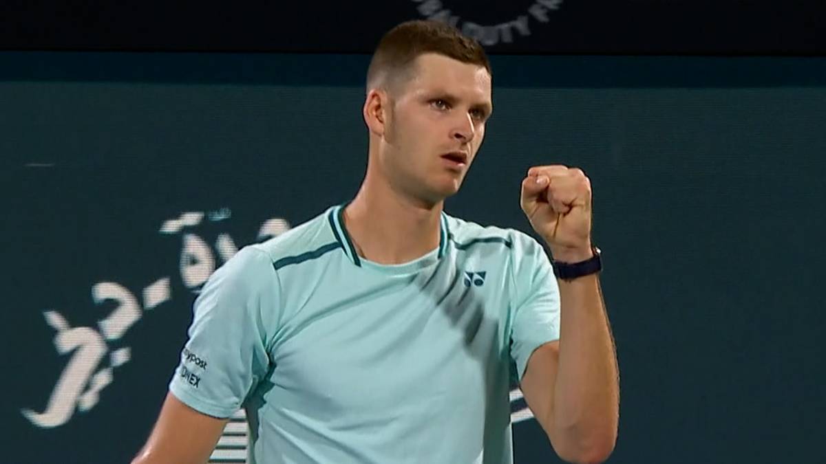 Hubert Hurkacz podczas meczu tenisowego, ubrany w jasnoniebieską koszulkę z zielonymi akcentami, zaciska prawą pięść w geście triumfu.