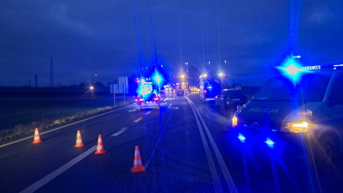 Zablokowana droga krajowa z migającymi niebieskimi światłami policyjnymi i pachołkami ostrzegawczymi.