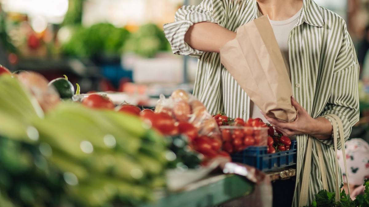 Osoba wybiera pomidory na targu spożywczym, trzymając papierową torbę.