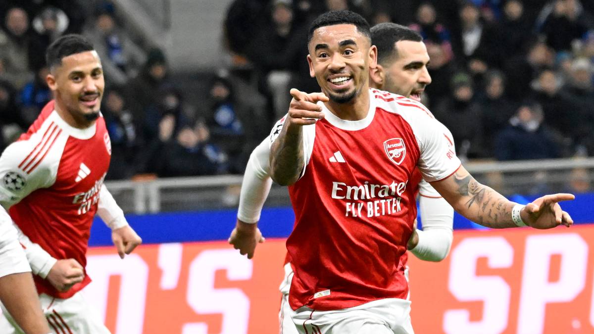 Piłkarz w czerwono-białej koszulce Arsenalu świętuje zdobycie bramki, wskazując palcem w stronę kamery. W tle widać innych zawodników i trybuny stadionu.