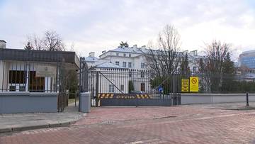 Brama wjazdowa do budynku z widocznym placem i drzewami w tle.