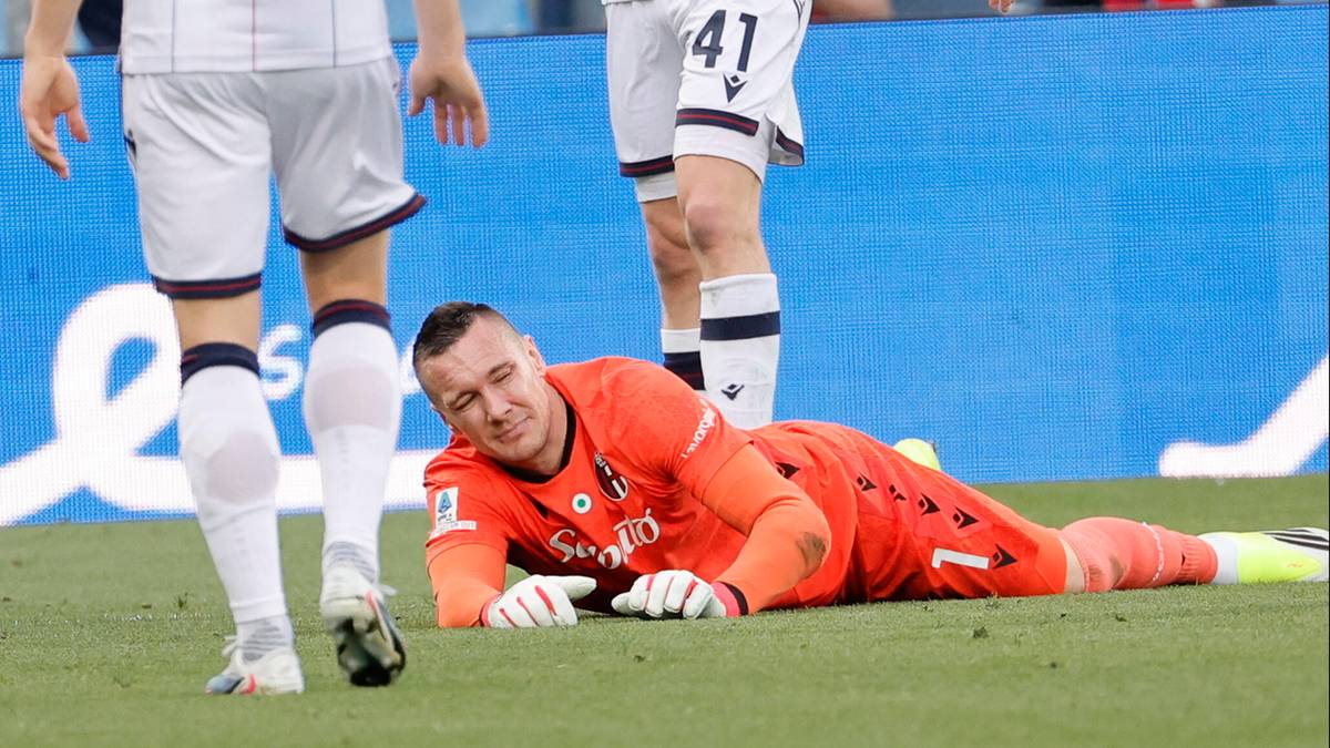 Piłkarze na boisku, jeden z nich leży na trawie.