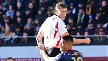 Dw&oacute;ch piłkarzy walczy o piłkę w powietrzu podczas meczu piłki nożnej.