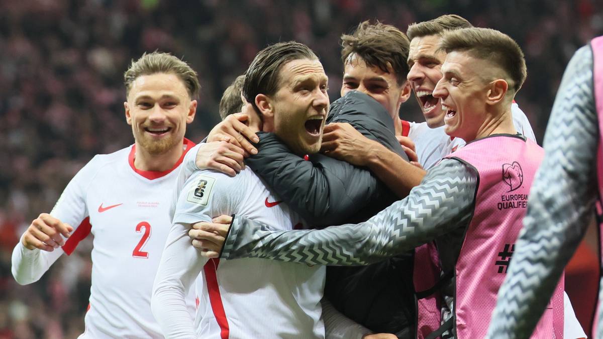 Piłkarze reprezentacji Polski w białych i czerwonych strojach świętują radośnie na boisku piłkarskim.