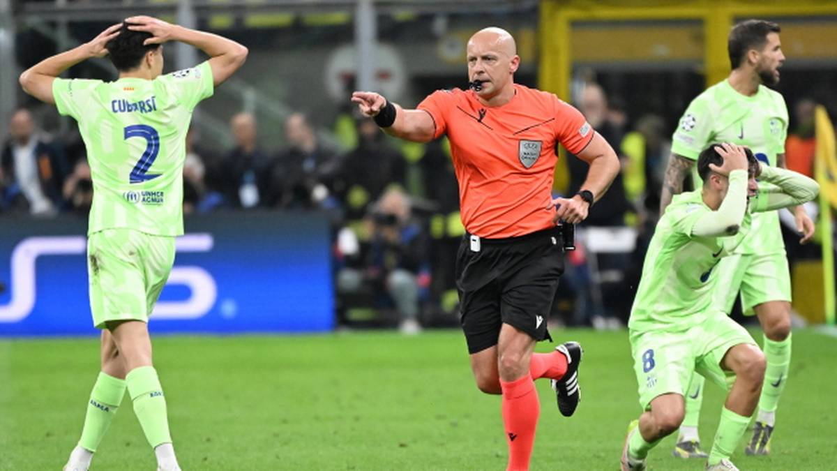 Sędzia piłkarski w pomarańczowej koszulce z numerem 3 i czarnych spodenkach wskazuje palcem w kierunku boiska. Po jego lewej stronie klęczy zawodnik w zielonej koszulce, trzymający się za głowę, a po prawej stoi inny zawodnik w zielonej koszulce z numerem 2.