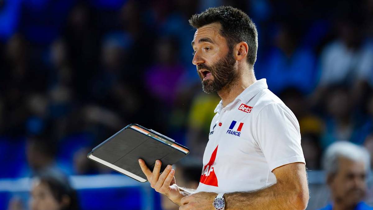 Mężczyzna w białej koszulce z flagą Francji, trzymający tablet, podczas meczu siatkówki.