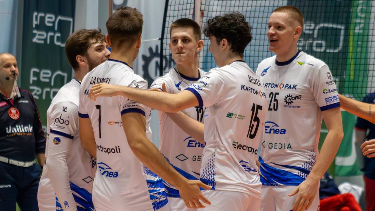 Grupa siatkarzy w białych strojach świętuje na boisku, trzymając się nawzajem.