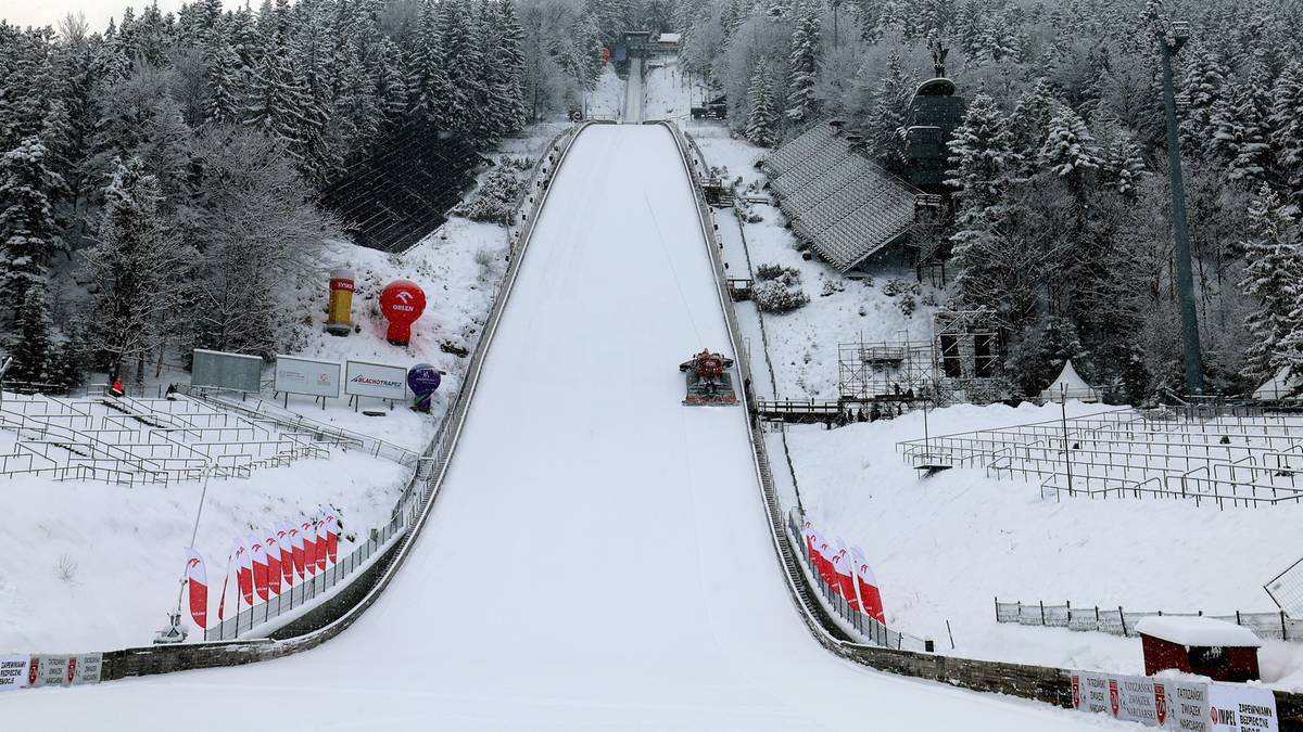Zimowa skocznia narciarska pokryta śniegiem, otoczona lasem iglastym.