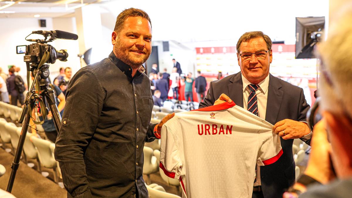 Dw&oacute;ch mężczyzn pozuje do zdjęcia, jeden z nich trzyma białą koszulkę z napisem "URBAN".