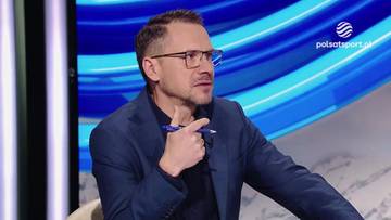 Mężczyzna w okularach i granatowej marynarce z długopisem w dłoni, udzielający wywiadu w studiu telewizyjnym.