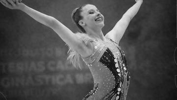 Młoda gimnastyczka artystyczna w stroju sportowym z uniesionymi ramionami.