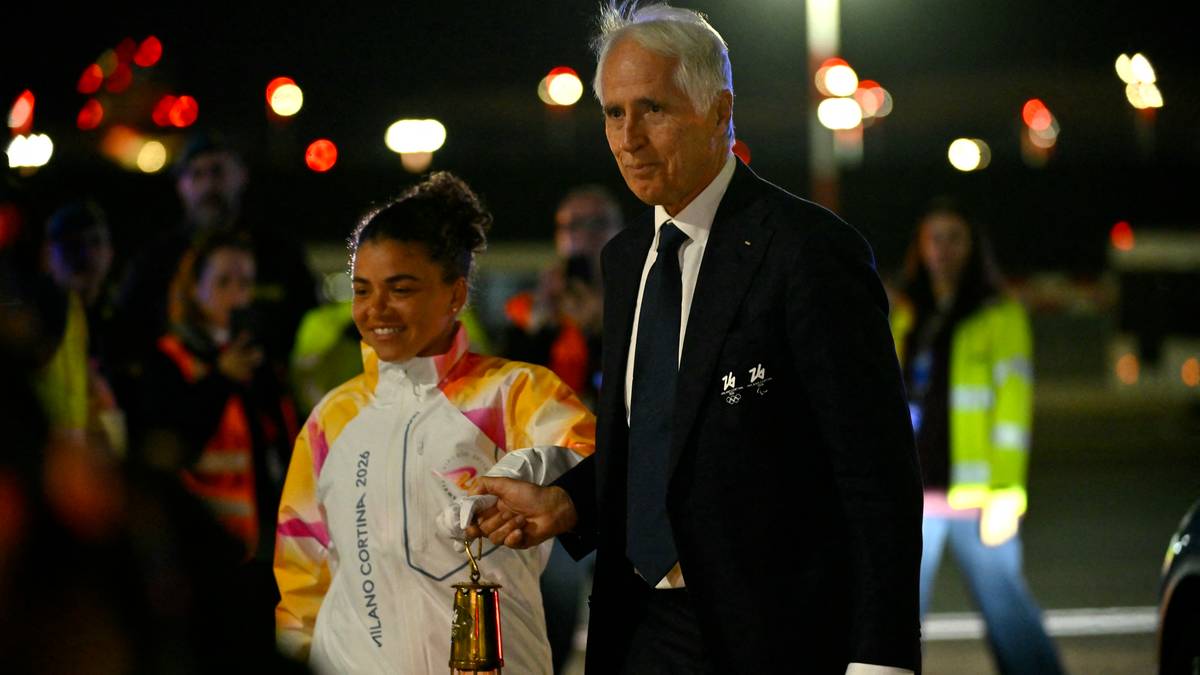 Jasmine Paolini trzyma olimpijski ogień, prowadzona przez mężczyznę w garniturze.