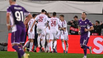 Piłkarze w białych i fioletowych strojach świętujący bramkę na boisku.