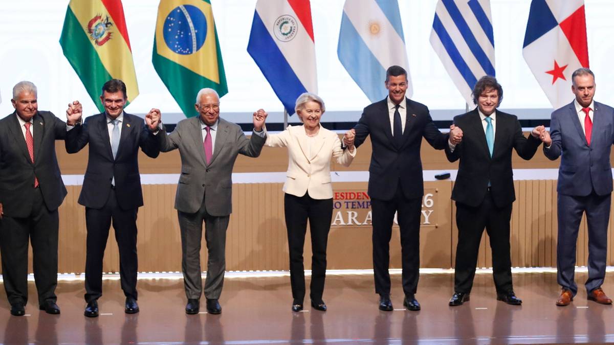 Grupa os&oacute;b pozuje do zdjęcia na tle flag Unii Europejskiej i kraj&oacute;w Mercosur.