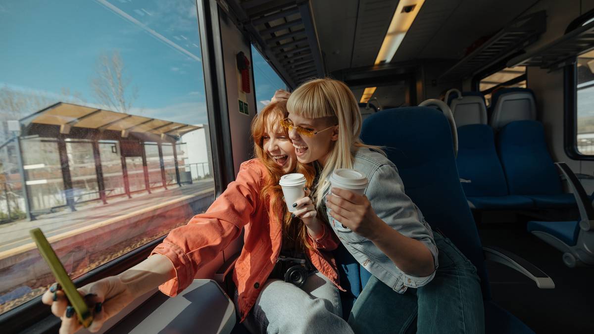 Dwie kobiety siedzą obok siebie w pociągu, pijąc kawę i patrząc przez okno.