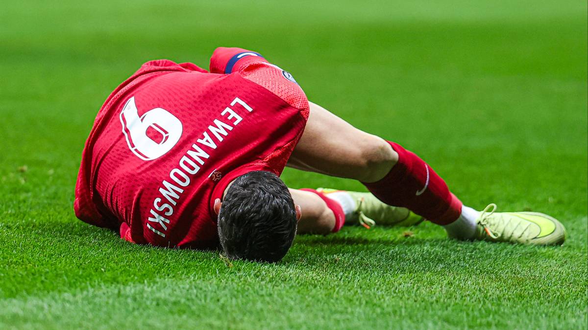 Piłkarz w czerwonej koszulce z numerem 9 leży na trawie, trzymając się za nogę.