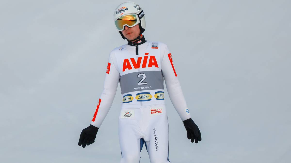 Skoczek narciarski w białym kombinezonie z czerwonymi wstawkami i numerem 2