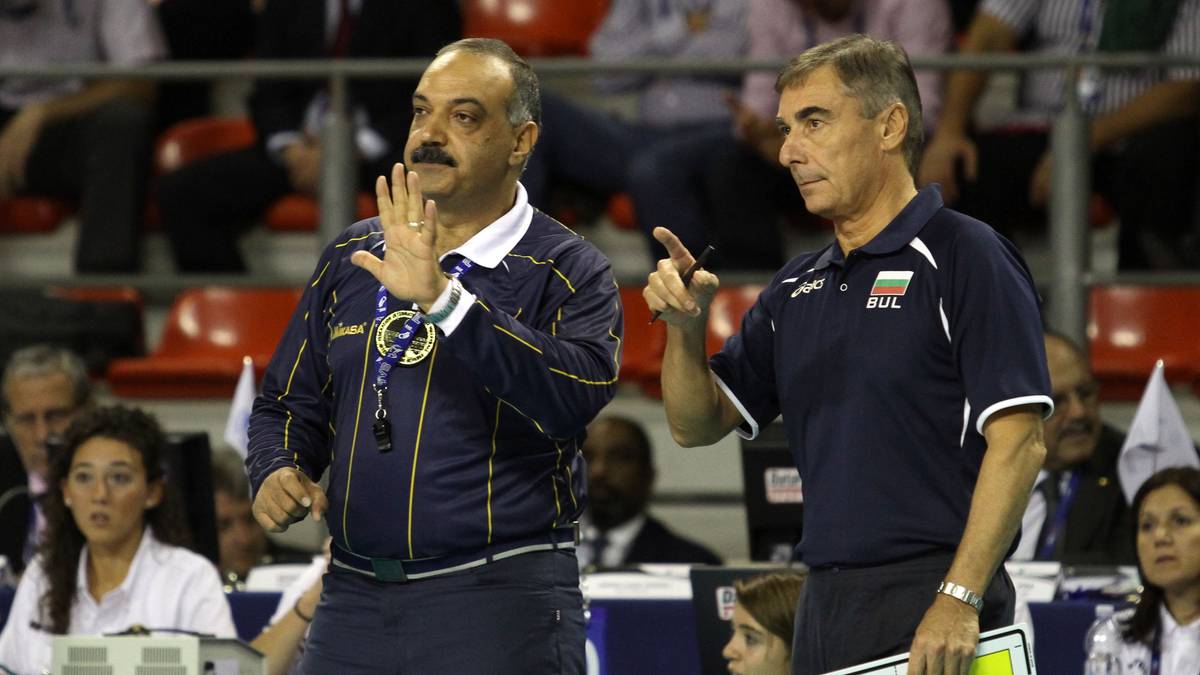 Dw&oacute;ch mężczyzn, prawdopodobnie trener&oacute;w sportowych, rozmawia i gestykuluje podczas meczu. Jeden z nich trzyma tablicę taktyczną.