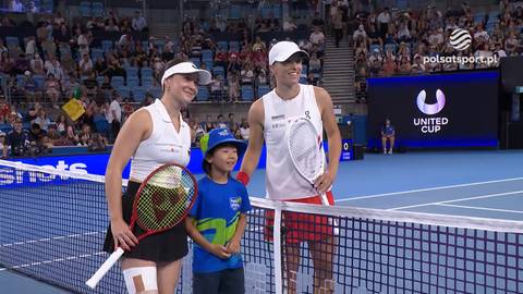 Iga Świątek i Eva Lys stoją na korcie tenisowym z chłopcem, obie trzymają rakiety tenisowe.