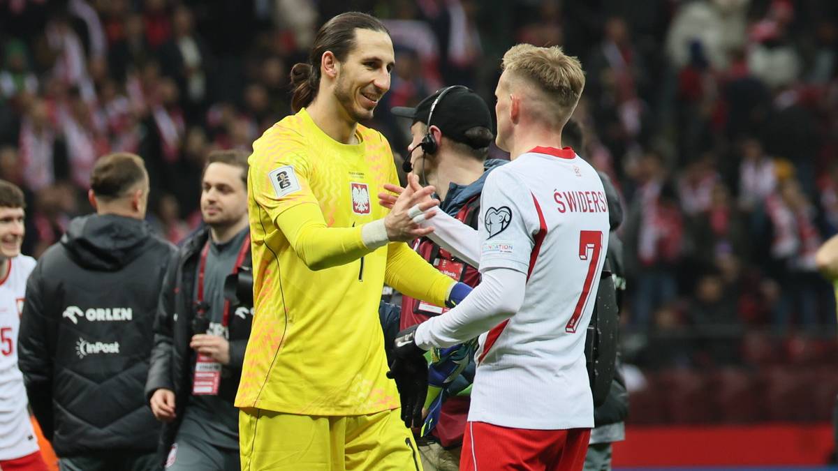 Piłkarze reprezentacji Polski podczas meczu, jeden w żółtym stroju bramkarza, drugi w białej koszulce, podają sobie ręce na murawie stadionu.