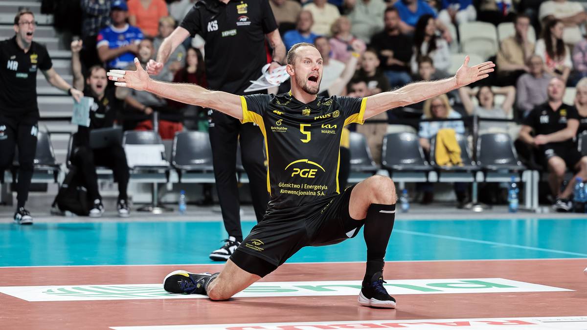 Siatkarz w akcji na boisku, klęczący z wyrazem triumfu na twarzy.