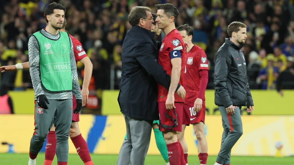 Robert Lewandowski w otoczeniu trenera i innych piłkarzy po przegranym meczu.