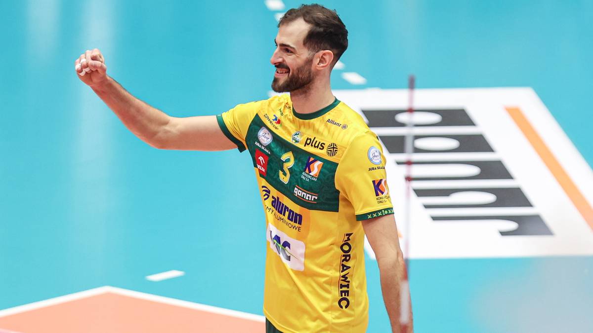 Siatkarz w ż&oacute;łtej koszulce z numerem 3, z uniesioną prawą ręką w geście zwycięstwa, na boisku siatkarskim.