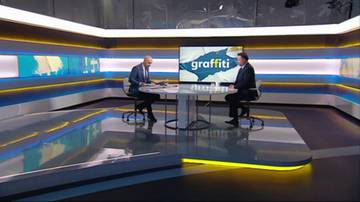 Dwóch mężczyzn w garniturach siedzi przy okrągłym stole w studiu telewizyjnym. Na ekranie w tle widnieje napis "graffiti".