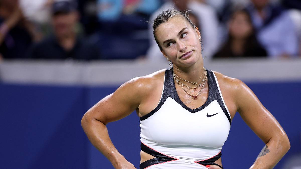 Aryna Sabalenka, zawodniczka tenisa, podczas meczu, w białym stroju sportowym, z rękami na biodrach.