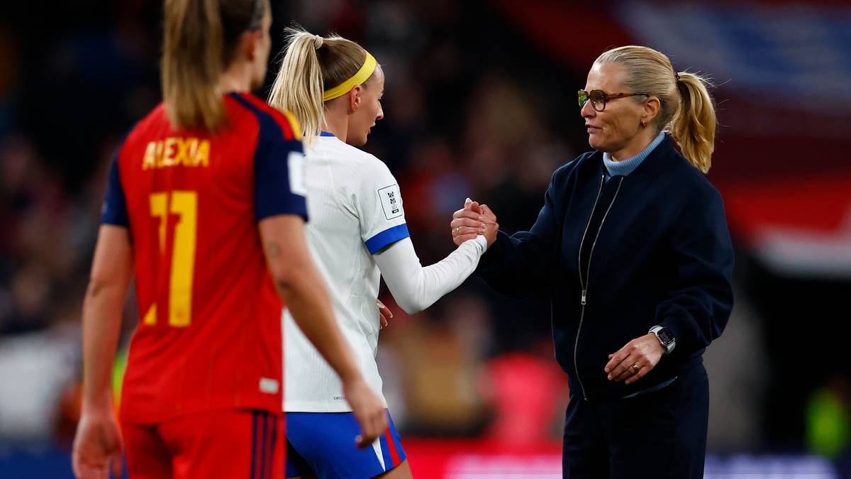 Trzy kobiety w strojach piłkarskich na boisku, jedna podaje rękę drugiej.