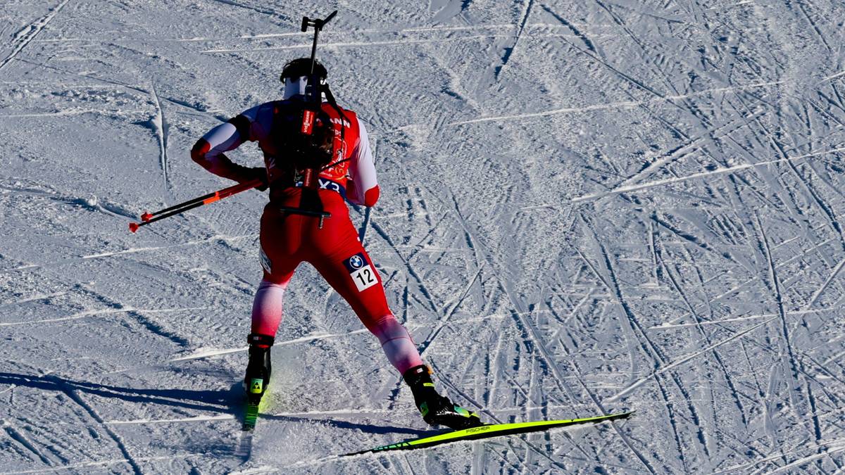 Biathlonista w czerwonym stroju na nartach, z karabinem na plecach, na ośnieżonym stoku.