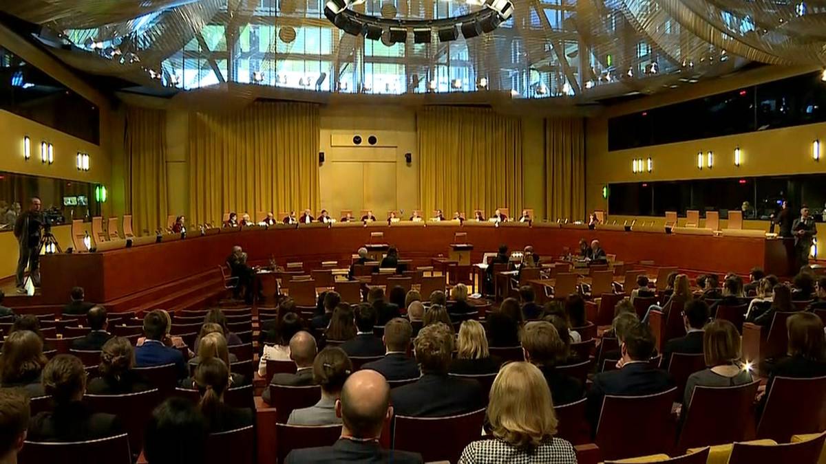 Widok na wnętrze sali sądowej z widownią w dolnej części kadru i panel sędziowski na podwyższeniu w tle.