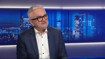 Mężczyzna w okularach i marynarce siedzi przed ekranem z widokiem nocnego miasta.