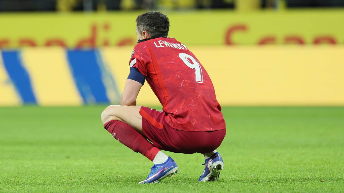 Robert Lewandowski w czerwonej koszulce z numerem 9 siedzi na murawie stadionu.