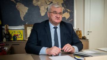 Mężczyzna w garniturze siedzi przy biurku przed mapą świata.